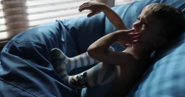 Küçük çocuk mavi koltuğa oturur ve ağlar. Çocuk gücendi ve ağladı.