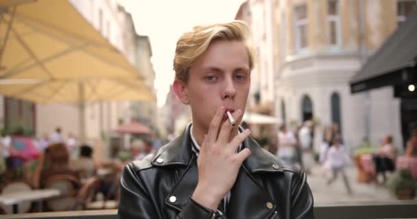 Портрет блондинки в чорній куртці, який курить цигарку на вулиці — стокове відео