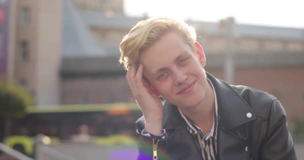 Giovane ragazzo biondo raddrizza i capelli e ride. il sole splende luminoso. bel tempo — Video Stock