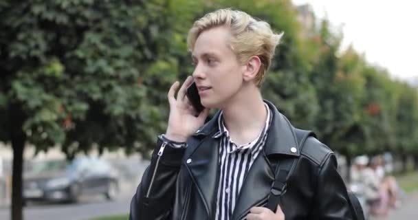 Молодий чоловік йде по вулиці і емоційно розмовляє по телефону. емоції при розмові по телефону — стокове відео