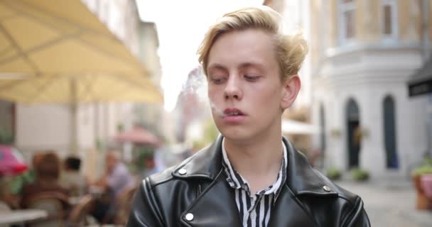 Szomorú szőke fickó áll és dohányzik az utcán.. — Stock videók