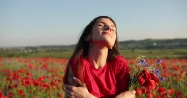 Haşhaş tarlasının ortasında kırmızı elbiseli, doğa güzeli bir kadın. Onun mükemmel kumral, uzun saçları rüzgarda uçarken güneş ışınları onun üzerinde parlıyor.