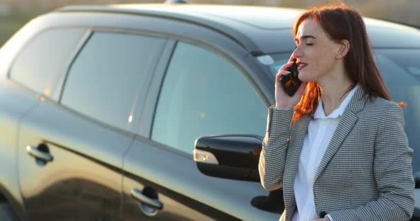 Όμορφη επιχειρηματίας μιλάει στο κινητό τηλέφωνο και χαμογελά. Στέκεται κοντά στο αυτοκίνητό της και κοιτάζει προς τα εμπρός με χαρά. — Αρχείο Βίντεο