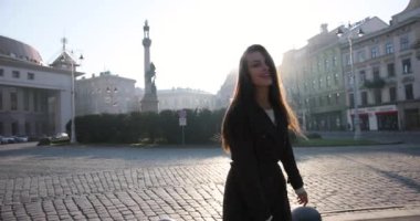 Kahverengi ceketli, gülümseyen çekici kadın güneşli bir havada sokakta yürüyor. Gülümsüyor, daireler çiziyor ve mükemmel kumral saçlarıyla oynuyor.