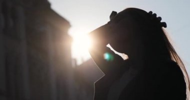 Uzun esmer saçlı çekici bir kadın silueti güneş ışınları onu aydınlatırken sokakta kalıyor. Güneş eski binadan parlıyor, mavi gökyüzünden.