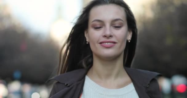 Faszinierender Blick einer unglaublichen brünetten Frau. Lächelnde attraktive Dame im braunen Mantel geht bei sonnigem Wetter durch eine Gasse — Stockvideo