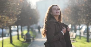 Çekici esmer kadın yapraksız ağaçlarla dolu sokakta yürüyor, kameraya dönüyor ve inanılmaz görünüşüyle büyülüyor.