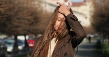 Kahverengi ceketli, kendine güvenen bir kadının Portret 'ı bir ara sokakta yürüyor ve güneşli havada saçlarıyla oynuyor. Arkaplanda kentsel ayarlar