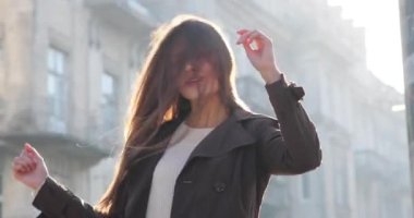 Çekici esmer kadın eğleniyor. Sokakta oturuyor, başını sallıyor, saçlarıyla oynuyor ve kameraya bakıyor. Rüzgar esiyor ve saçları dalgalanıyor. Güneş ışınları parlıyor