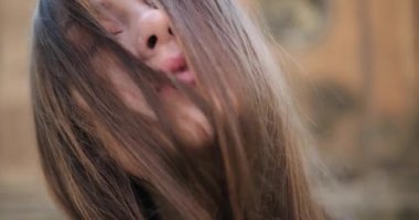 Güzel mavi gözlü, kumral, uzun saçlı güzel genç bayana yakından bakın. Kameraya bakar ve saçıyla oynar. Sokak, güneşli gün