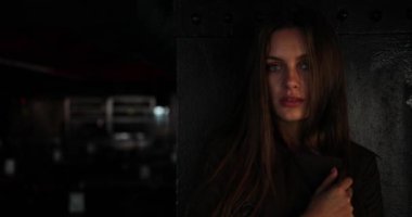 Esmer kadın, tenha bir restoranda, siyah metal duvarın yanında kalıyor. Kameraya bakıyor ve inanılmaz görünüşüyle büyülüyor. Işık odası