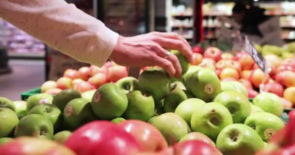 Una gran selección de manzanas en el supermercado. joven atractivo hombre con barba elige manzanas en el supermercado. hombre de camisa blanca olfateando manzana verde — Vídeo de stock