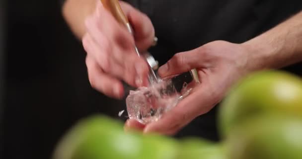 Close-up χέρια μπάρμαν με παγοθραυστικό συνθλίβει τον πάγο για κοκτέιλ στο παρασκήνιο των πράσινων μήλων. — Αρχείο Βίντεο