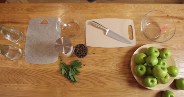 위에서 본 모습. 요리사가 식탁으로 와서 딜을 도마 위에 올려 놓습니다. 식탁 위에는 후추 열매, 소금, 사과와 만 잎 한 병, 칼, 도마, 물통 과 유리그릇 이 있다 — 비디오