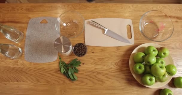 Vue de dessus. le chef vient à la table et met l'aneth sur la planche à découper. sur la table sont des grains de poivre, un pot de sel, pommes et feuilles de laurier, couteau, planche à découper, bouteilles d'eau et bols en verre — Video