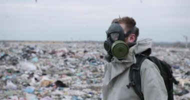 Koruyucu kostüm ve gaz maskeli bir adam atık alanı kirliliği, ekolojik felaket yakınlarında yürüyor..