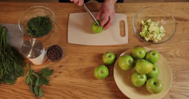 Top view. mens hands cut green apple. on the wooden table are peppercorns, a jar of salt, apples and bay leaves, knife, cutting board, water bottles and glass bowls. spices. — Stock Video