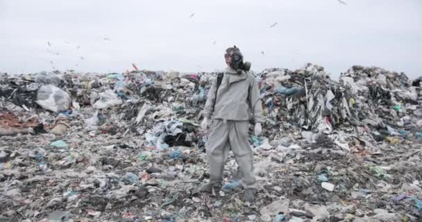 Un uomo con una maschera antigas sta tra le discariche e tiene in mano un ramo con delle cime. disastro ecologico. inquinamento. — Video Stock