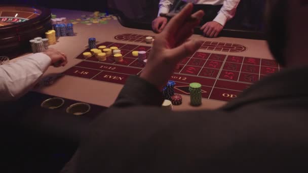 Der Dealer im Casino nimmt alle Jetons mit seinen Händen vom Spieltisch auf. Eine Gruppe Männer sitzt hinter dem Roulettetisch im Casino, trinkt Whiskey und raucht Zigarren — Stockvideo
