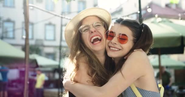 Ritratto di due belle ragazze allegre con sorrisi raggianti che abbracciano e ridono. due giovani donne attraenti felici in occhiali da sole — Video Stock