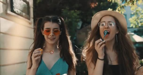 Zwei attraktive, glückliche Freundinnen gehen eine Stadtstraße entlang und blasen Seifenblasen auf. zwei schöne Mädchen. attraktive Freundinnen — Stockvideo