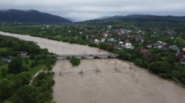 Güzel Karpat dağları ve dağ kasabasının arka planındaki yağmurlardan sonra kıyılardan yükselen dağ nehri.