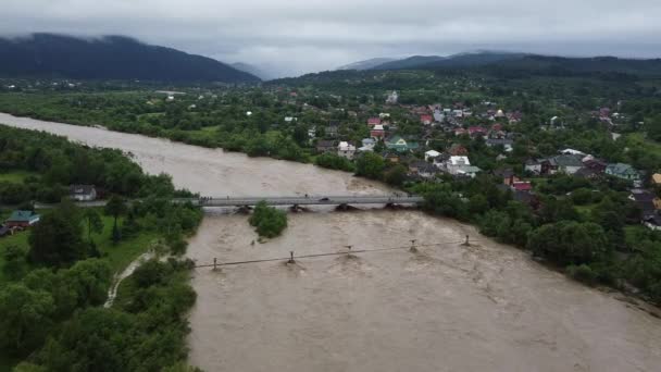 Gebirgsfluss, der nach den Regenfällen vor dem Hintergrund der wunderschönen Karpaten und der Bergstadt aus den Ufern kam — Stockvideo