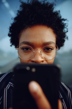4 bin. Modern çizgili takım elbiseli çekici Afrikalı Amerikalı kadın. Telefonunu tutarken kameraya bakıyor. İş kadını ya da öğrenci. Kapat..