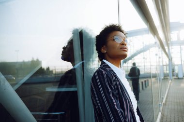 4 bin. Seyahat et, Dijital. Zarif çizgili takım elbiseli, bavullu Afro-Amerikan bir kadın. Cam duvara yaslanmış ve uçuşunu bekliyor. İş kadını ya da öğrenci. Ve gökyüzüne bakar