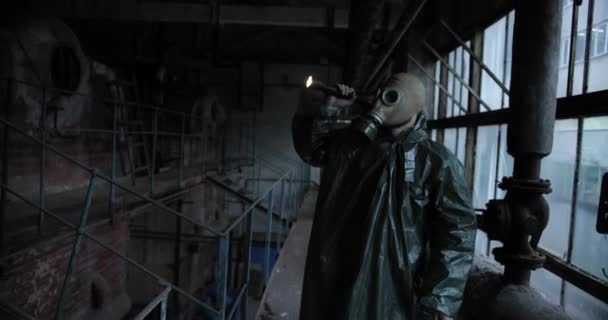 Людина в захисному одязі з ліхтариком і газовою маскою йде на покинуті заводські приміщення. людина в газовій масці дивиться на покинуту кімнату — стокове відео