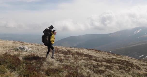 Молодая женщина путешественник с большим рюкзаком в желтой куртке с видом на удивительные горы и долину. Пространство для текста. Одетый в стильный осенний костюм бохо. — стоковое видео