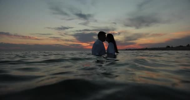 Silhouetter af mand og kvinde i kærlighed kysse på solnedgangen. De ser på hinanden og mand kysser kvinde på baggrund af orange gradient af solnedgang himmel. Kærlig par kysse dykning ind i – Stock-video