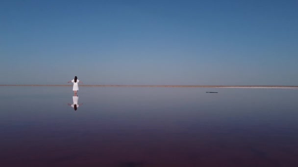 Spiegelbild im Wasser einer Frau im weißen Kleid. Glückliche Frau auf einem rosa Salzsee an einem sonnigen Sommertag — Stockvideo