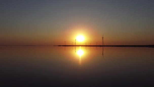 Große Rotorblätter einer Windkraftanlage vor dem Hintergrund eines orangen Sonnenuntergangs am Horizont mit heller Scheibensonne in Zeitlupe. Alternative Energiequellen. Windiger Park. Ökologische Energie — Stockvideo