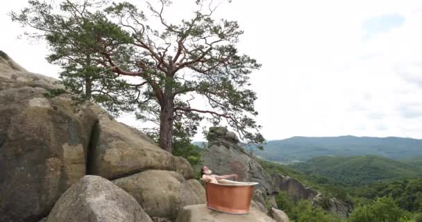 Homem velho com uma barba branca e cabelos grisalhos longos senta-se na banheira na rocha sob uma árvore em um fundo de bela natureza — Vídeo de Stock