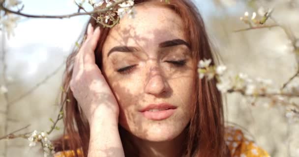 Close-up portret van charmant meisje met sproeten op gezicht met gesloten ogen, in het voorjaar tussen bloeiende boomtakken — Stockvideo