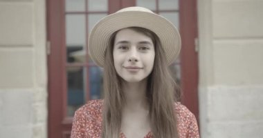 Uzun siyah saçlı, yaz şapkalı genç bir kadın gülümsüyor ve dışarıdaki kameraya bakıyor. Yakın plan portre.