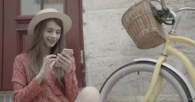 Çekici gülüşlü güzel esmer, bisikletin yanında otururken mutlu bir şekilde cep telefonunda sohbet ediyor ve geziniyor. 4k.