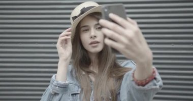 Çekici, kendine güvenen, şık şapkalı esmerin yakın plan portresi karanlık arka planda cep telefonundan selfie çekiyor. 4k.