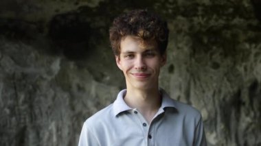 Genç adam kameraya bakıyor. Yalnız genç kız, açık havada. Yakından bakınca yakışıklının yüzü. Duvarda kıvırcık saçlı bir adam. Yakın çekim genç yüzü..