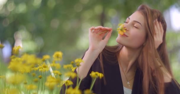 Gyönyörű fiatal szőke lány természetes smink és álmodozó megjelenés szép mosolygós, miközben élvezi és illata sárga virág a virágos kertben. — Stock videók