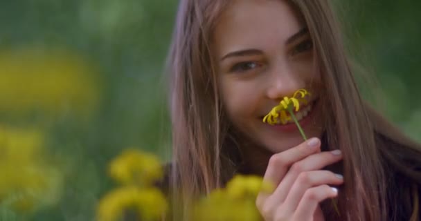 Adorável jovem loira com maquiagem natural é adorável sorrindo e cheirando a flor amarela no jardim florido. Movendo-se no cabelo do vento. — Vídeo de Stock