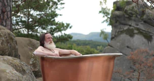 Starý muž s šedivými vousy odpočívá v koupelně venku — Stock video