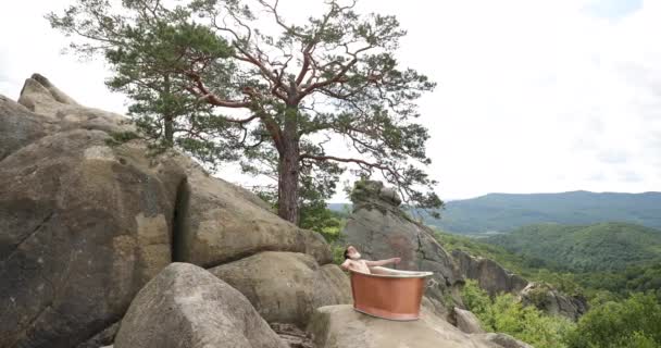 一个像圣诞老人这样的老人坐在山上的铸铁浴室里，悠闲自在地躺在外面美丽的风景里 — 图库视频影像