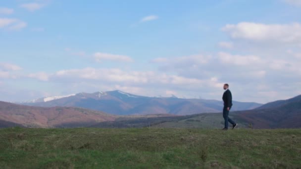 En ung mann i dress går langs et vakkert landskap i fjellene.. – stockvideo