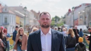 Bir adam şehir caddesinde bir insan deresinde duruyor ve doğrudan kameraya bakıyor..