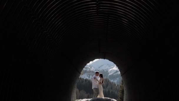 Vista de túnel sobre os beijos de casal amorosos na paisagem de montanhas cobertas de neve. Noiva e noivo em um passeio de casamento no fundo da montanha. — Vídeo de Stock