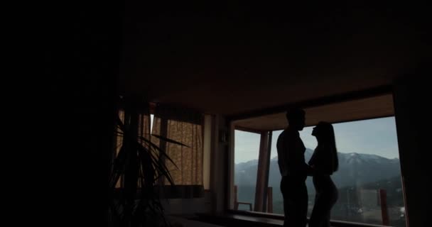 Nacktes junges Paar übernachtet in der Nähe der Fenster mit unglaublichem Panorama auf schneebedeckten Bergen und küsst sich. Holzhaus in den Bergen — Stockvideo