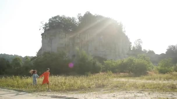 Pria muda yang bahagia dan wanita muda berjalan di luar ruangan, dengan latar belakang alam yang indah, berpegangan tangan. Pakaian olahraga yang bagus untuk anak muda.. — Stok Video