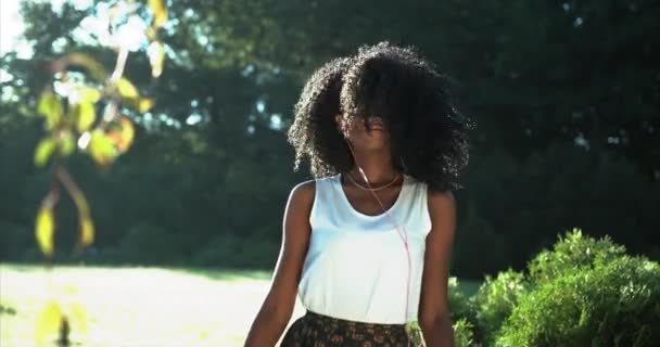 Energiczny taniec na świeżym powietrzu uroczej, młodej afro-amerykańskiej kobiety z zielonymi cieniami do powiek. Uśmiecha się i słucha muzyki w słuchawkach.. — Wideo stockowe